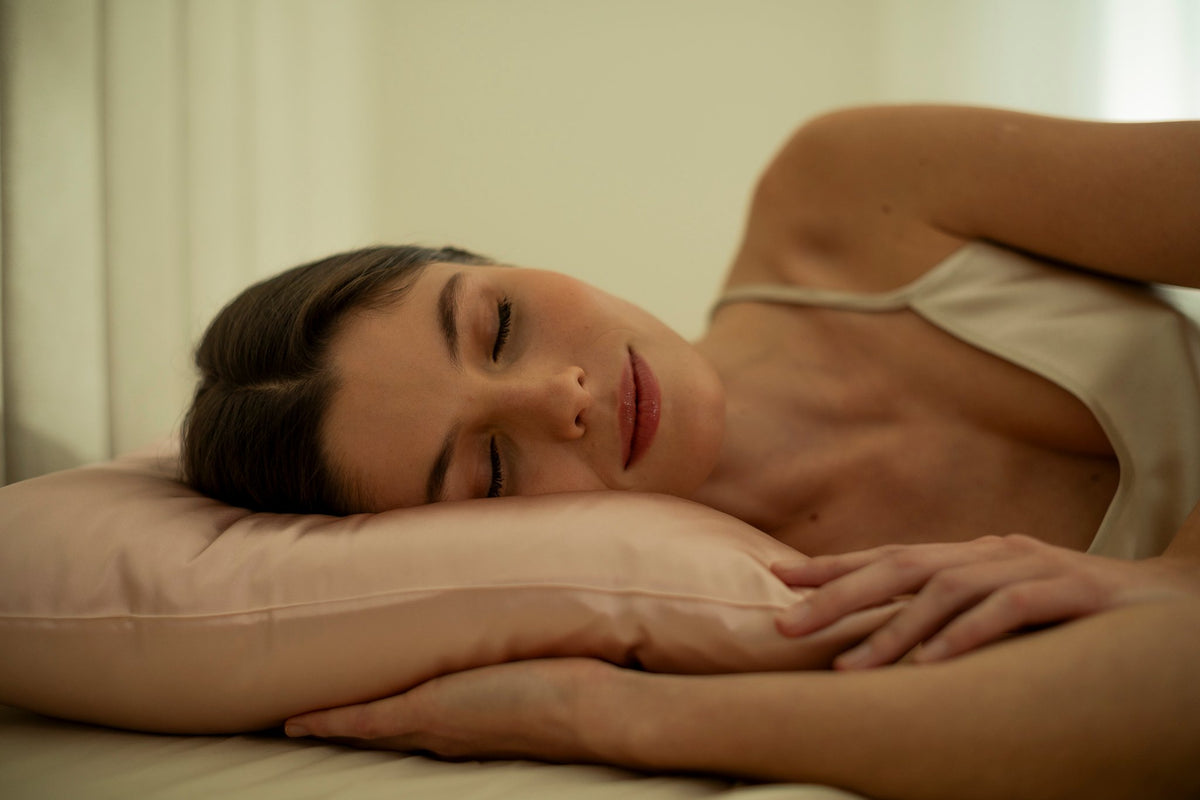 15. Woman lying on bed with pink silk pillowcase, emphasizing comfort and luxury