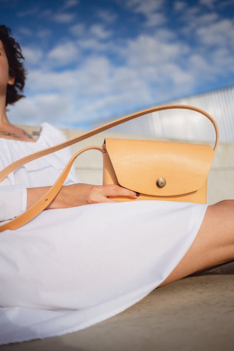 3. Mirgoods beige leather clutch held by woman in white dress, shown in outdoor setting