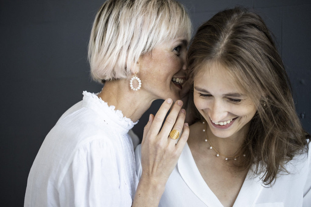 1. Two women sharing a moment, one wearing a gold Flower Of Life Ring by New Vintage by Kriss, showcasing its intricate design