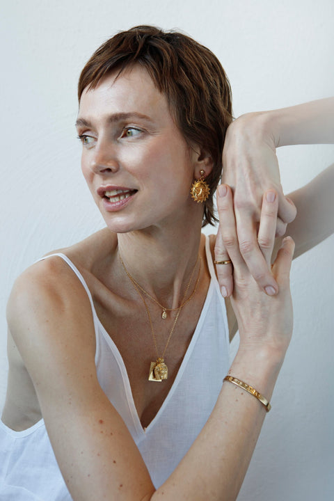 2. Woman wearing the Shine Bright Necklace by New Vintage by Kriss, featuring a gold-filled chain and Sun charm, styled with matching earrings and bracelet