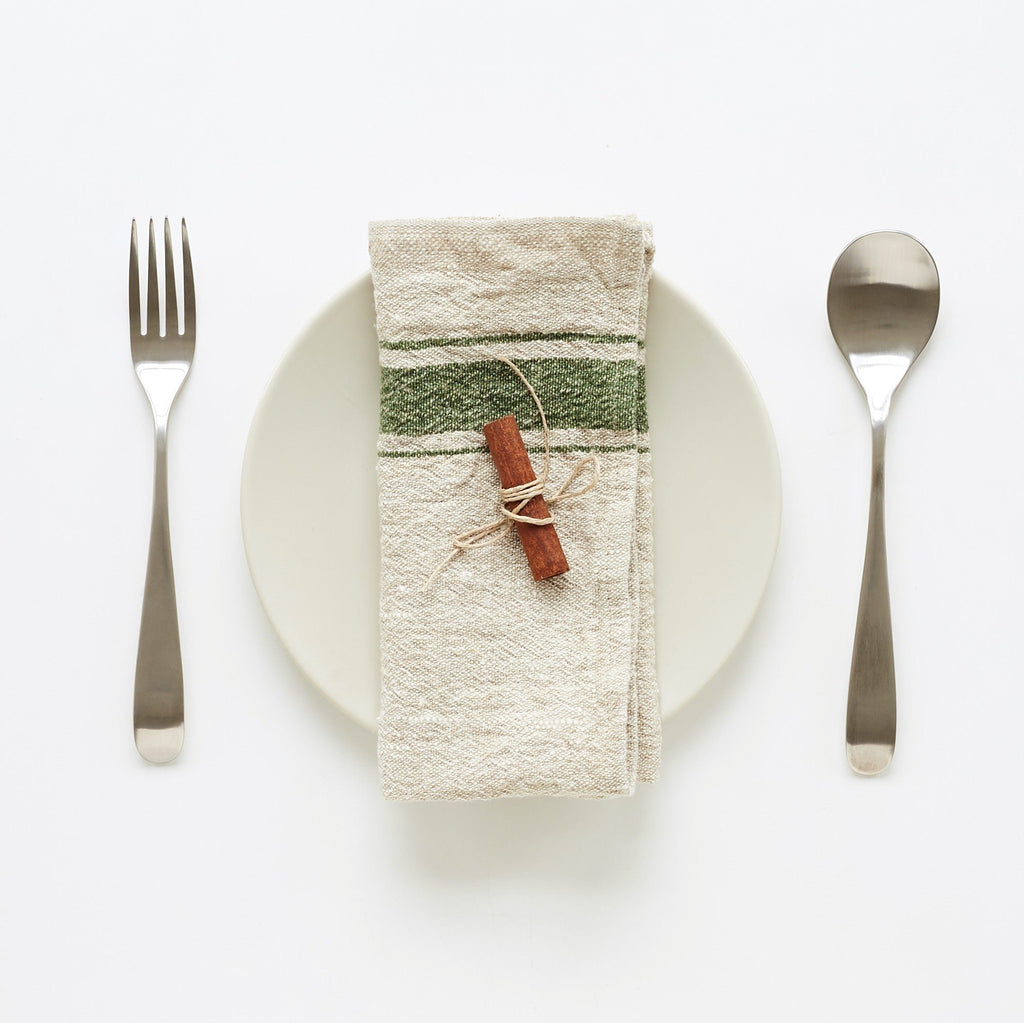 3. Green striped linen napkin on white plate with cinnamon stick, set with fork and spoon on white background