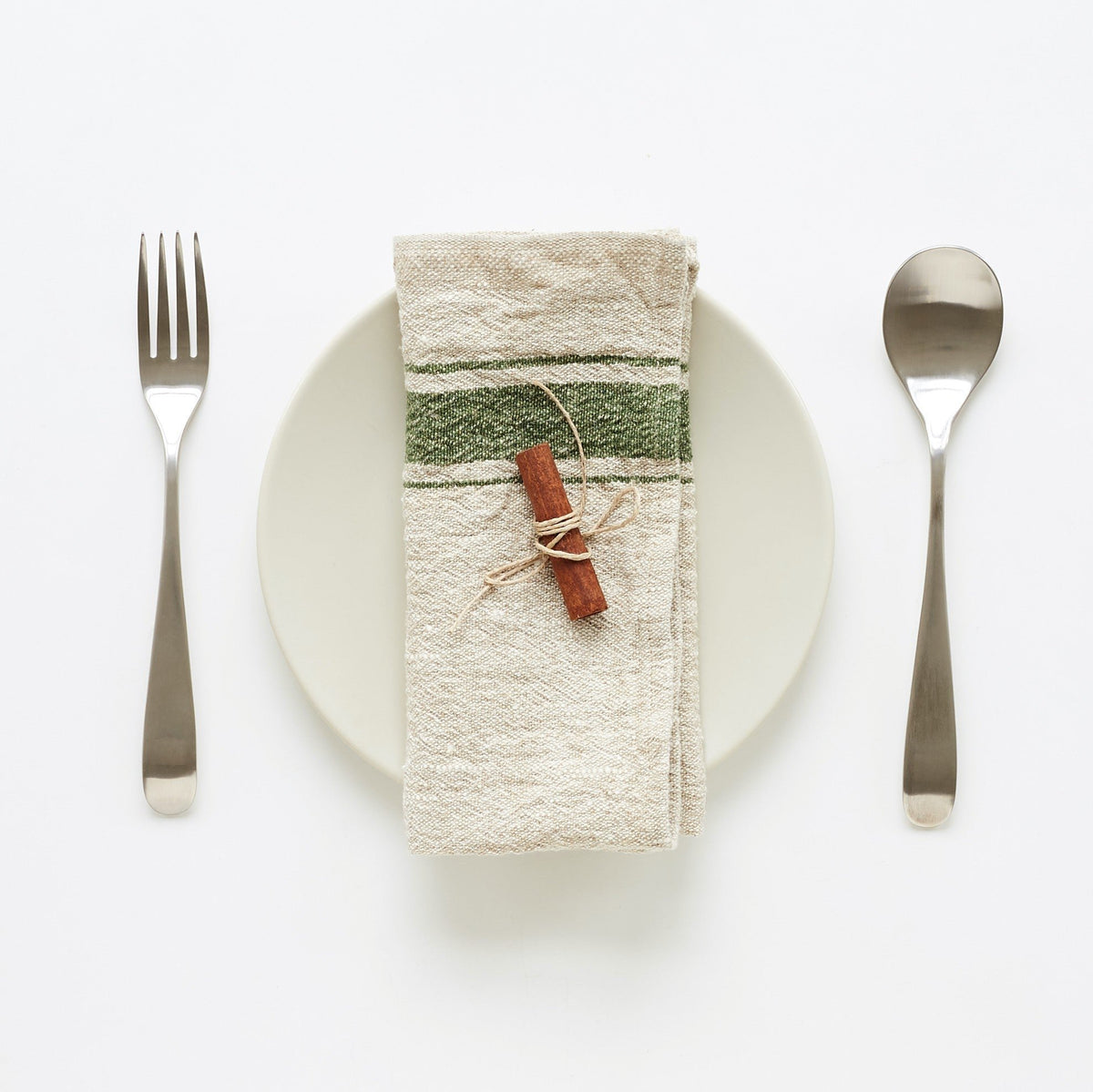 3. Green striped linen napkin on white plate with cinnamon stick, set with fork and spoon on white background