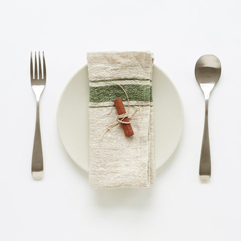 3. Green striped linen napkin on white plate with cinnamon stick, set with fork and spoon on white background