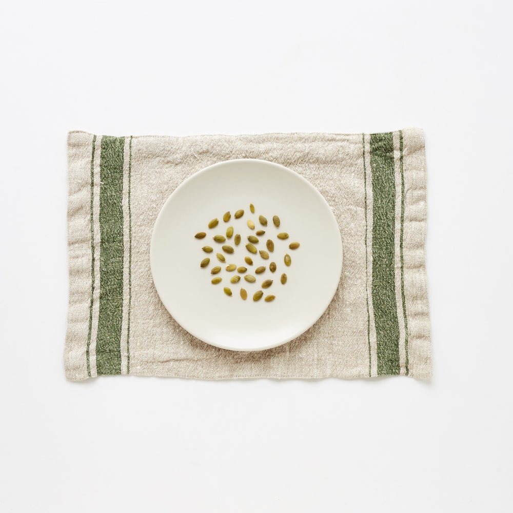 2. Green vintage stripe linen placemat with a white plate and pumpkin seeds on a white background