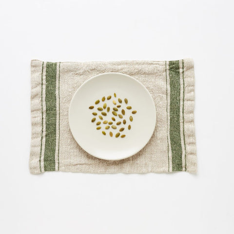 2. Green vintage stripe linen placemat with a white plate and pumpkin seeds on a white background