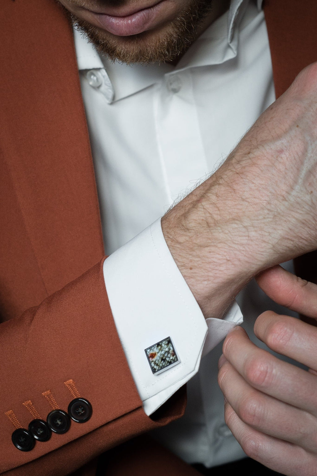 1. Man wearing white shirt and brown suit adjusting cuff with Eherüs square cufflink made from red-spotted brown trout leather