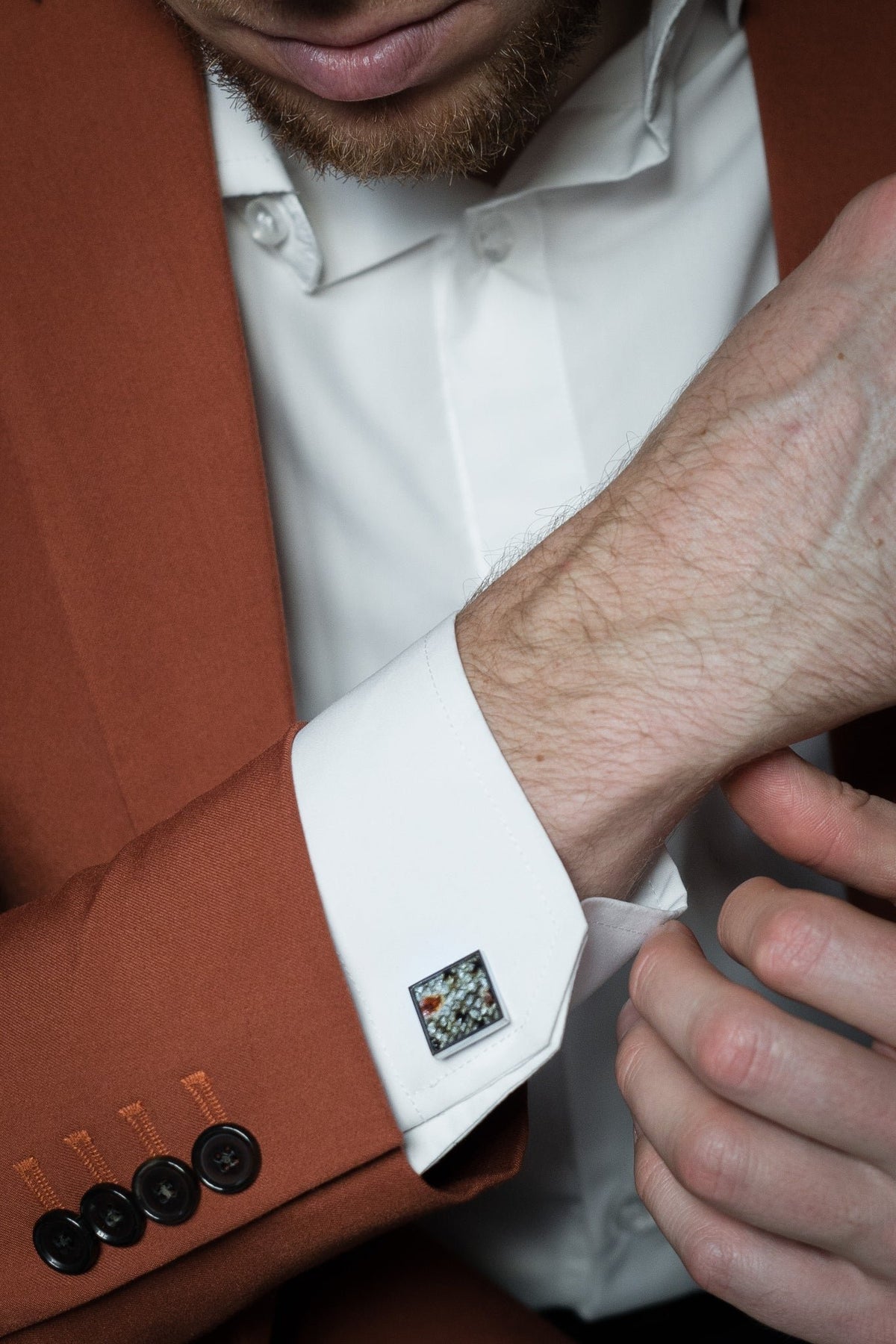 1. Man wearing white shirt and brown suit adjusting cuff with Eherüs square cufflink made from red-spotted brown trout leather