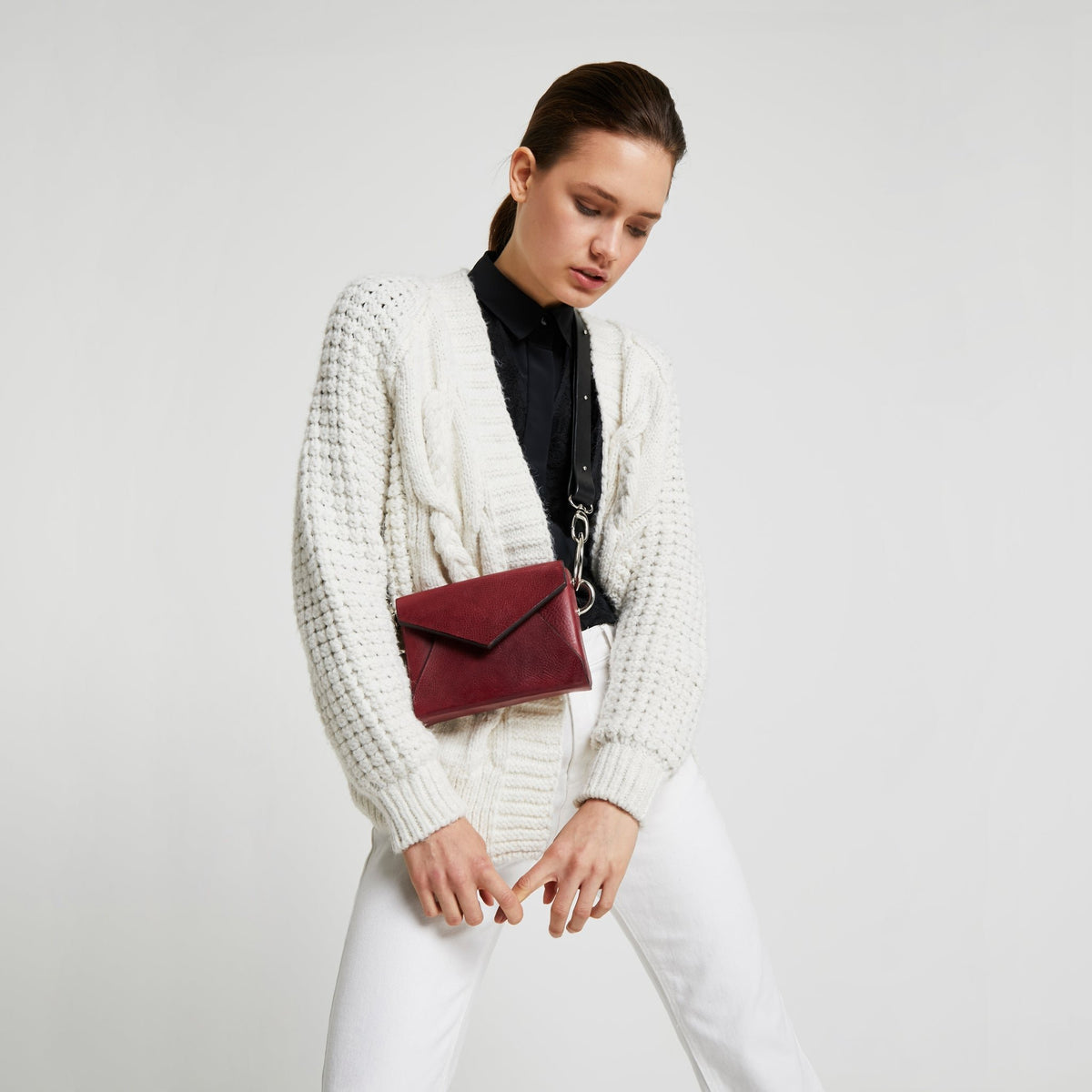 2. Woman showcasing Daz Studio burgundy leather envelope bag, worn crossbody with chic chain detail, in lifestyle setting