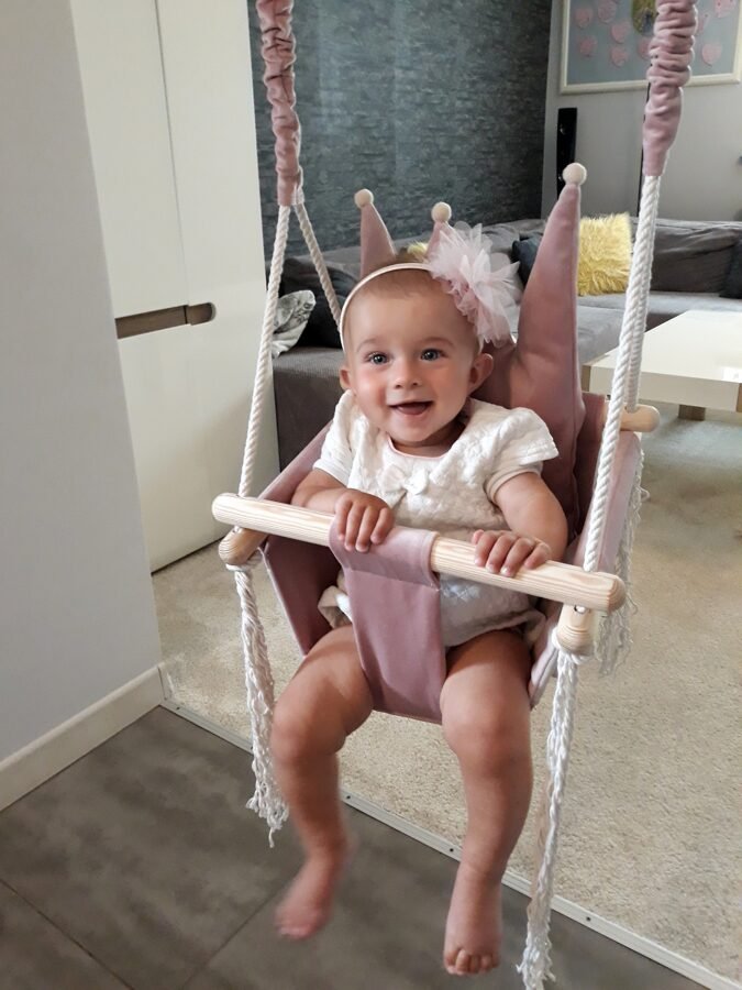 1. Baby in dusty pink crown-shaped swing with white outfit and headband in modern living room