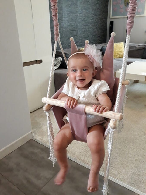1. Baby in dusty pink crown-shaped swing with white outfit and headband in modern living room