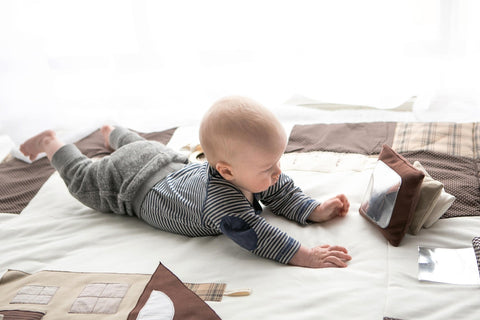 1. Baby reaching for Karloova Pillow Heap with mirror on brown pillow, lying on soft surface