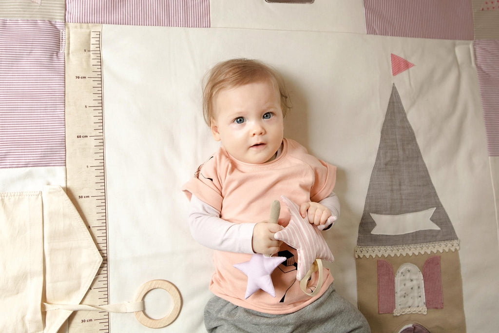 2. Baby in pink shirt holding starlet toy on a castle-themed play mat