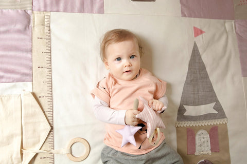 2. Baby in pink shirt holding starlet toy on a castle-themed play mat
