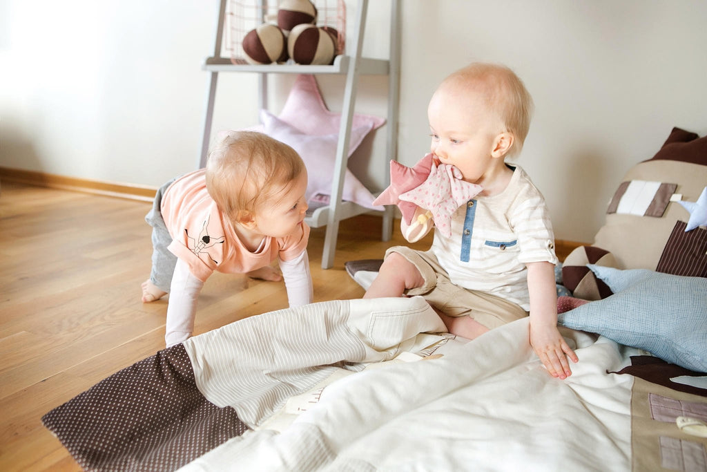 9. Two babies interacting, one holding pink starlet toy in a playroom