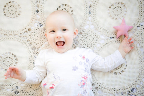 3. Laughing baby lying on crochet blanket holding pink star-shaped Karloova Magic Wand