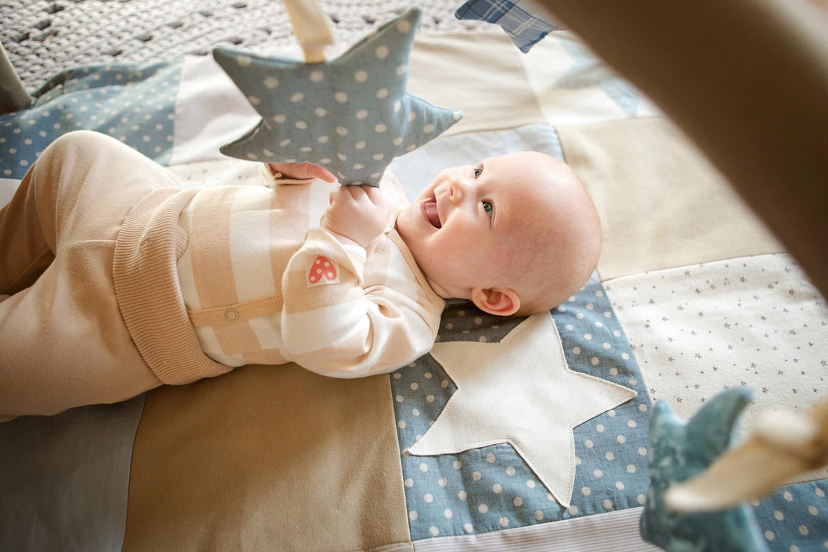 7. Baby smiling while holding blue polka dot starlet toy on play mat