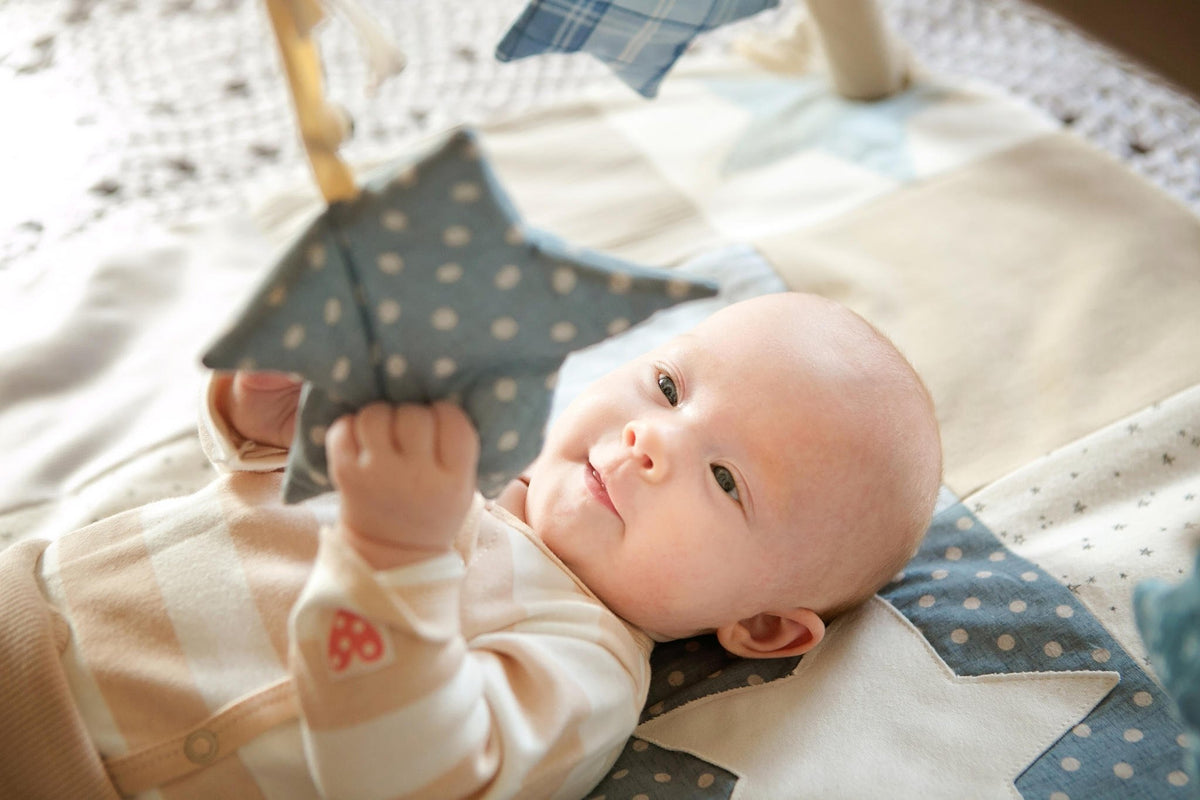 2. Baby gazing at blue polka dot star toy on Karloova activity mat