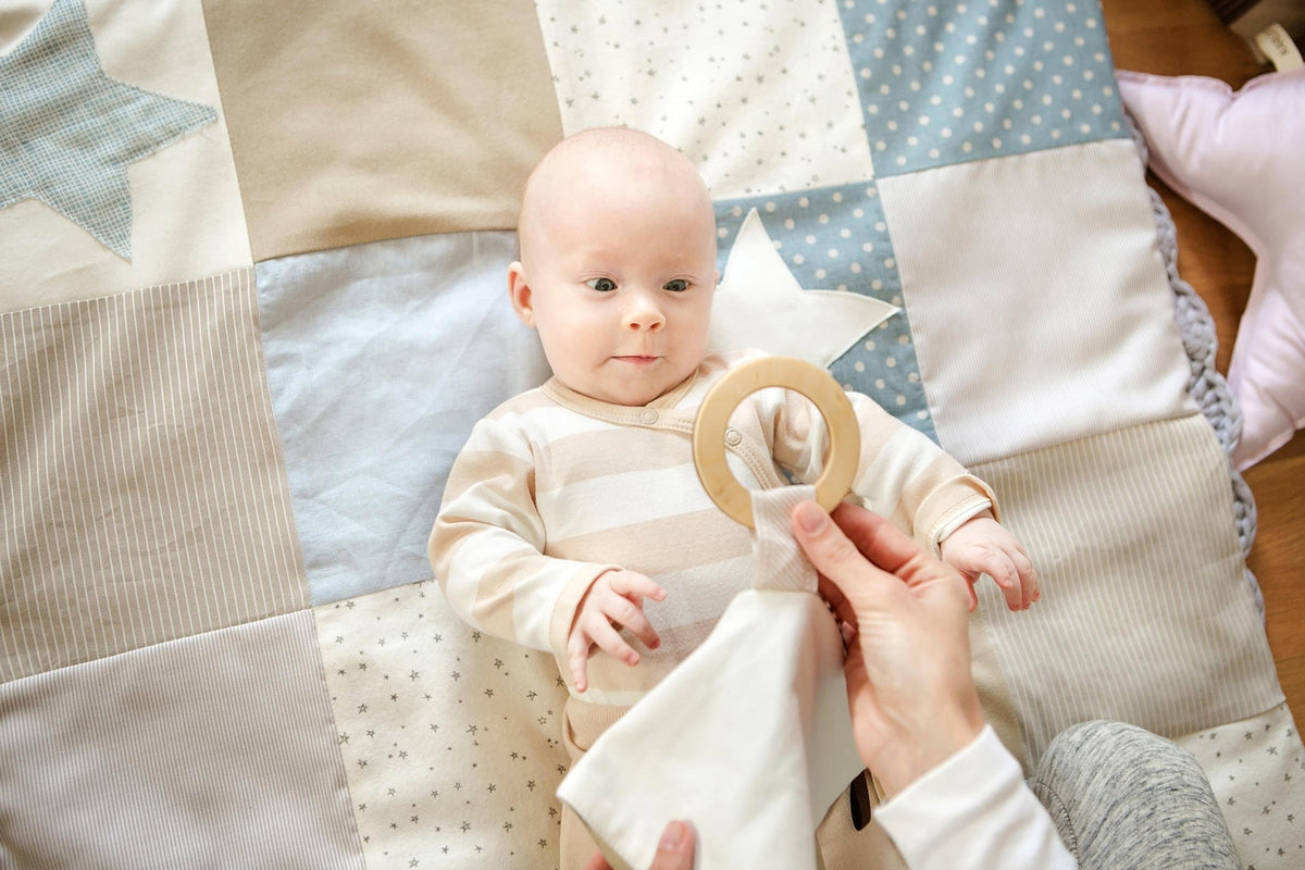 1. Baby on patchwork blanket interacting with Karloova comfort blanket featuring wooden hoop