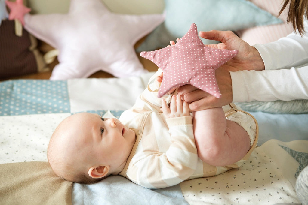 1. Baby holding pink polka dot starlet toy on a play mat with pastel colors