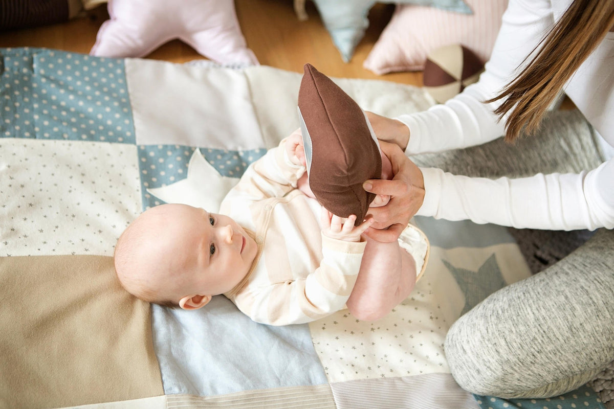 1. Baby holding brown pillow from Karloova Pillow Heap, assisted by adult on patterned mat