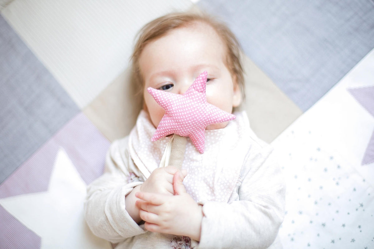 1. Baby holding pink star-shaped Karloova Magic Wand on patterned blanket
