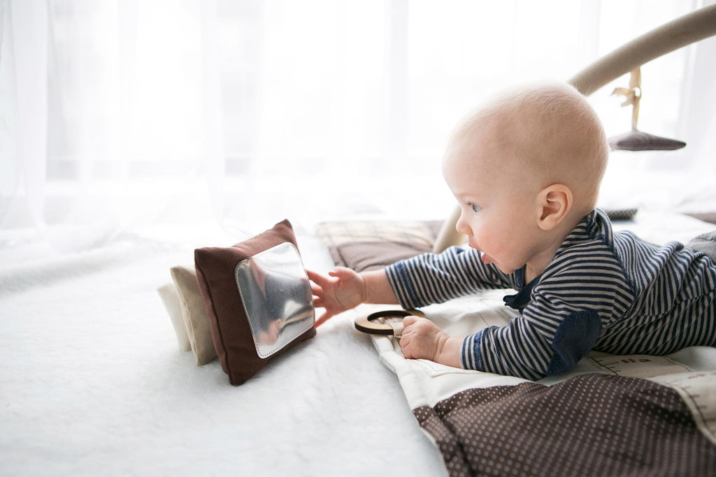 1. Baby reaching for Karloova Pillow Heap with mirror, lying on patterned blanket