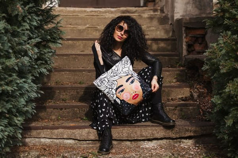 2. Woman sitting on steps with Garbanota HANDBAG YOKO in black, featuring unique graphic design