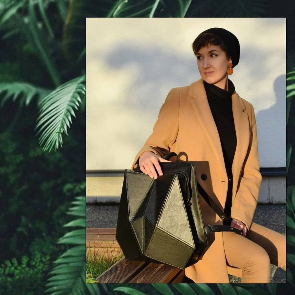 1. Woman sitting on bench with Gerda Retter Design FACET black leather backpack, showcasing Nordic minimalist style