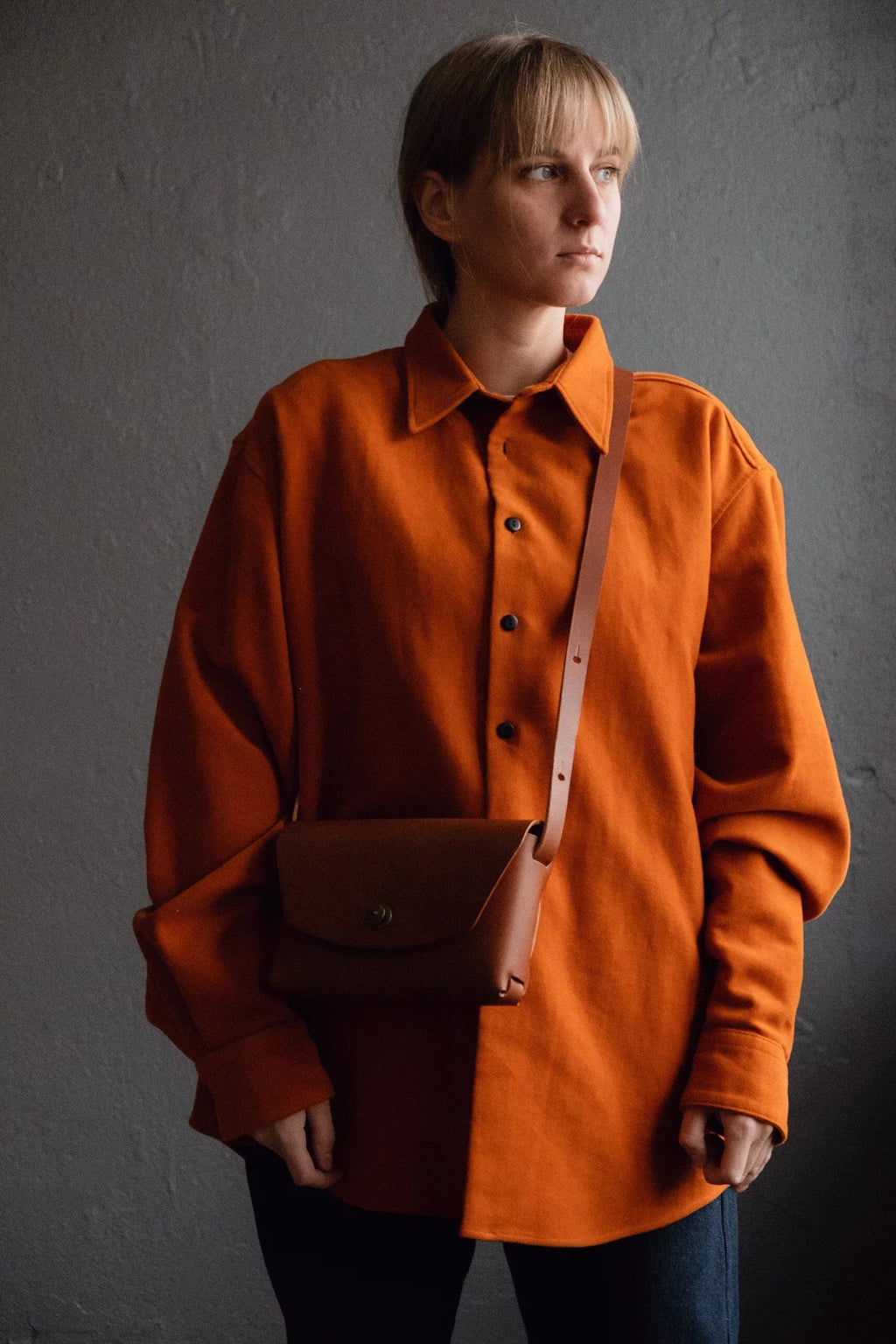 2. Handmade rust brown leather clutch by Mirgoods, styled with orange shirt, shown in studio