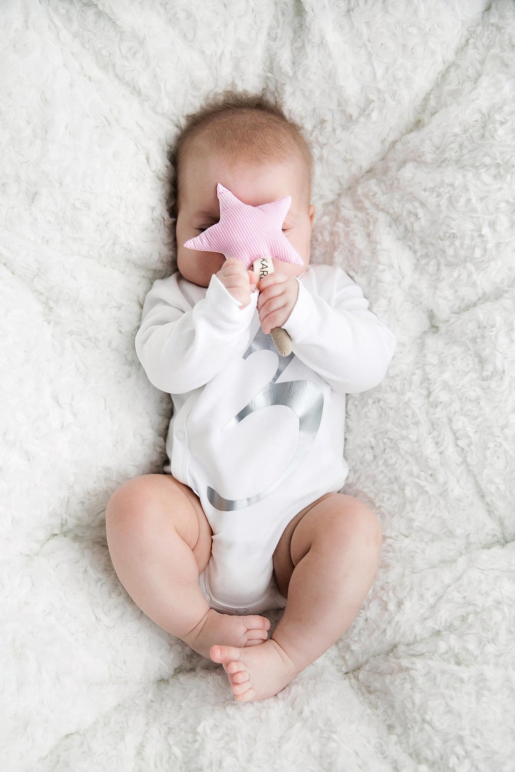 1. Baby lying on white blanket holding pink star-shaped Karloova magic wand