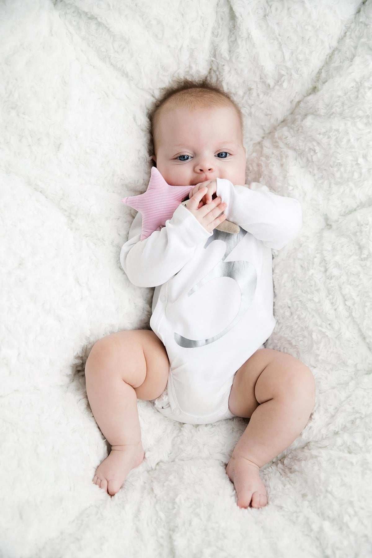 10. Baby in white onesie holding pink star-shaped Karloova Magic Wand on fluffy blanket