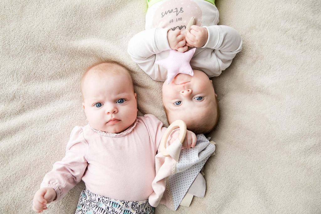 1. Two babies on beige blanket, one holding pink star-shaped Karloova magic wand