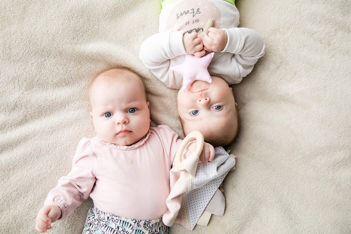 1. Two babies on beige blanket, one holding pink star-shaped Karloova magic wand