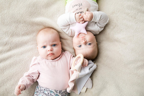 1. Two babies on beige blanket, one holding pink star-shaped Karloova magic wand