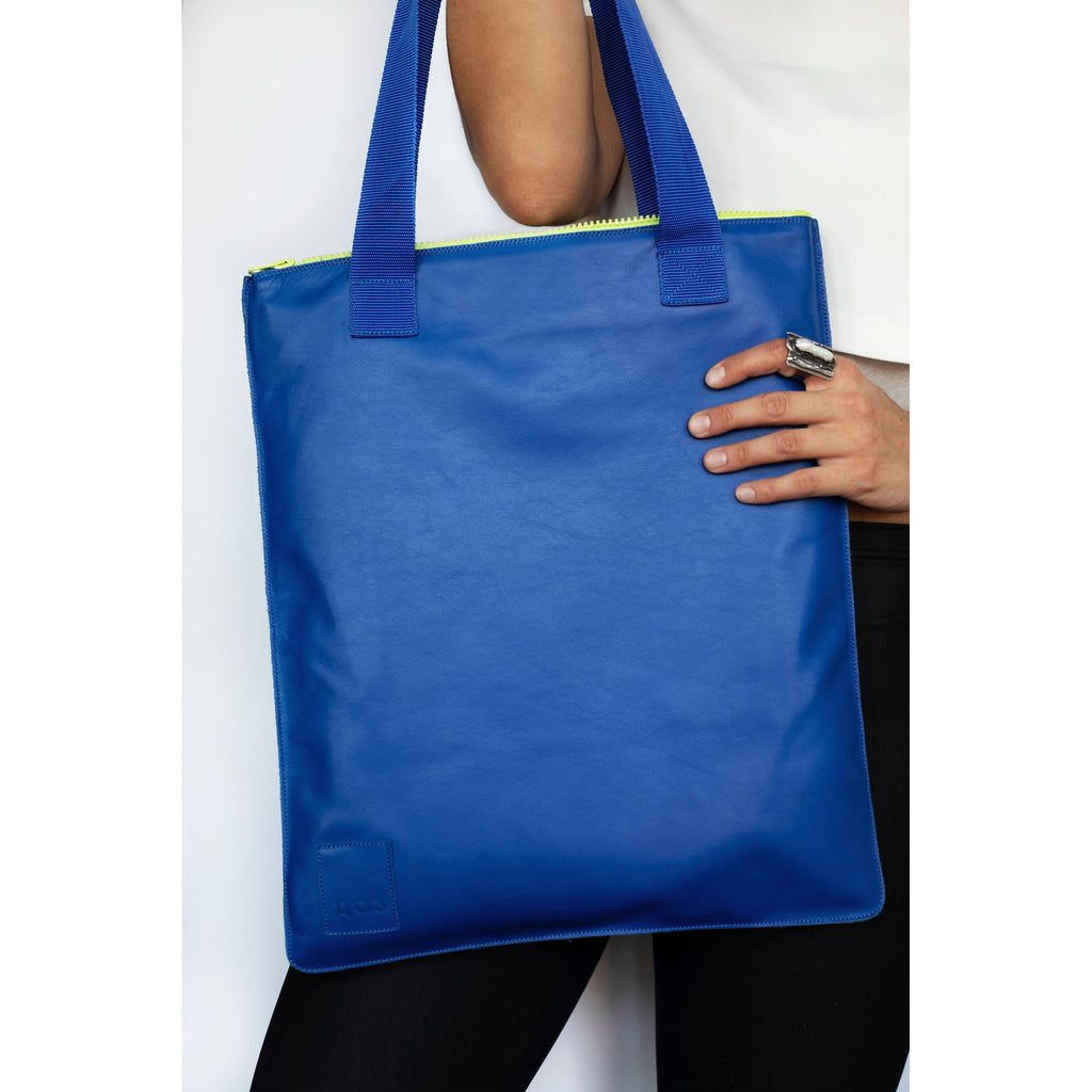 1. Woman holding Daz Studio handmade leather tote in royal blue with neon green zipper, styled with casual outfit