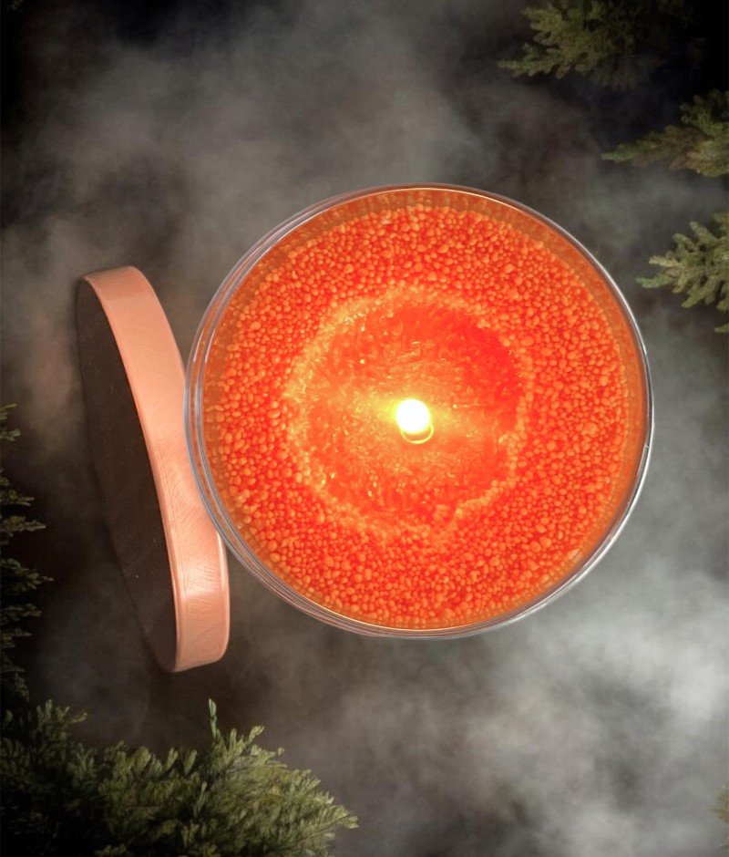 1. Top view of Candledust unscented powder candle in bold orange, lit in a glass container with lid, surrounded by mist