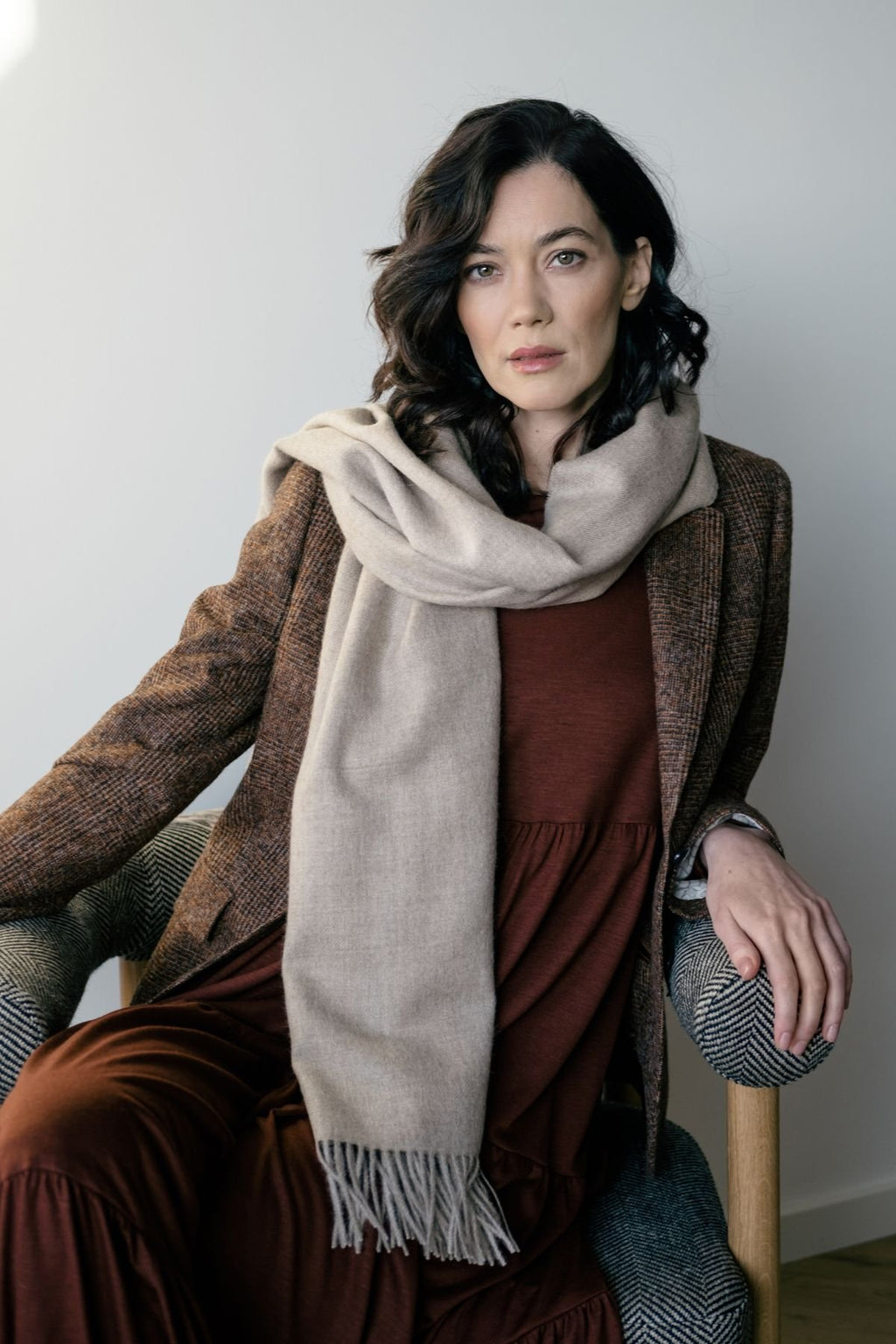 1. Woman wearing Alpaka natural baby alpaca maxi-scarf with fringes, styled with a brown coat in a lifestyle setting