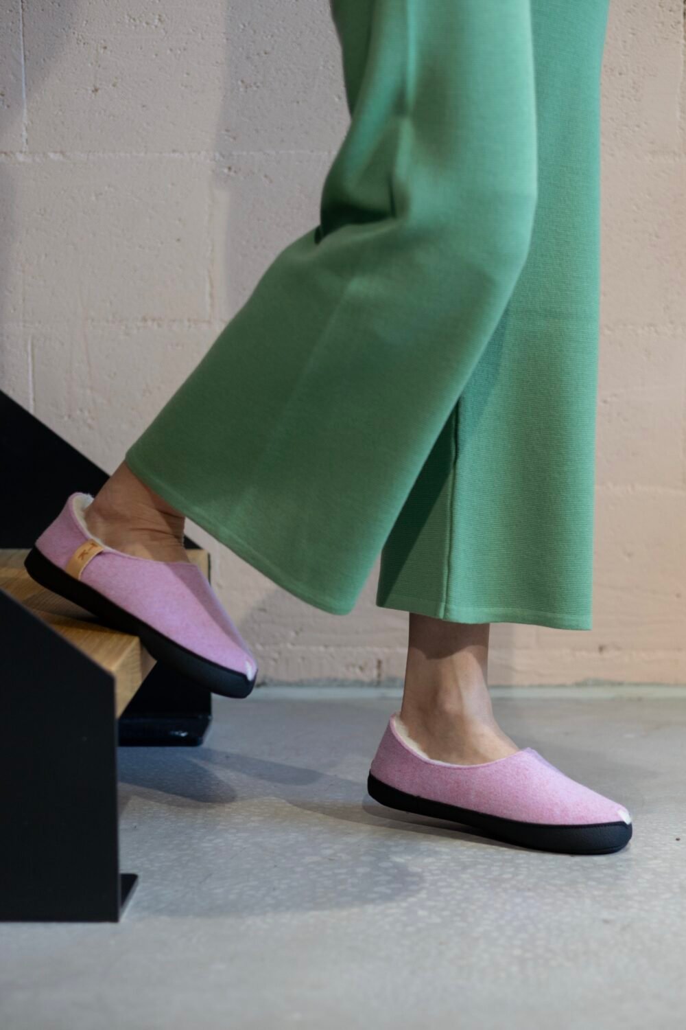 2. Woman stepping in TOKU Budapest light pink lambswool slippers, highlighting comfort and design