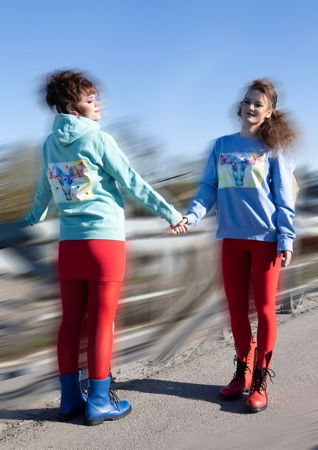 1. Two women holding hands wearing colorful sweatshirts and red leggings, one in blue boots, outdoors