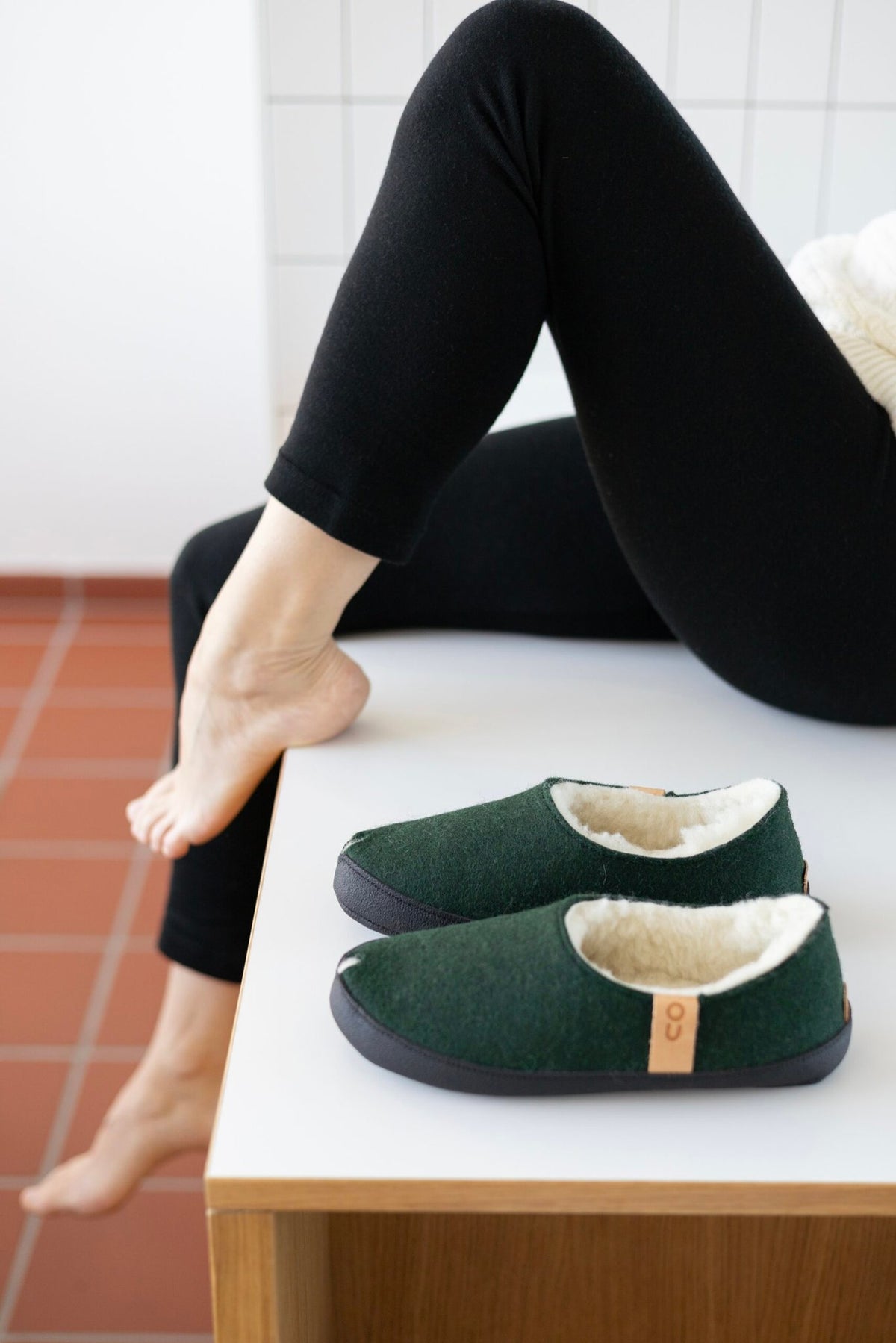 1. Unisex dark green TOKU Budapest slippers with lambswool lining, shown in lifestyle setting with model lounging