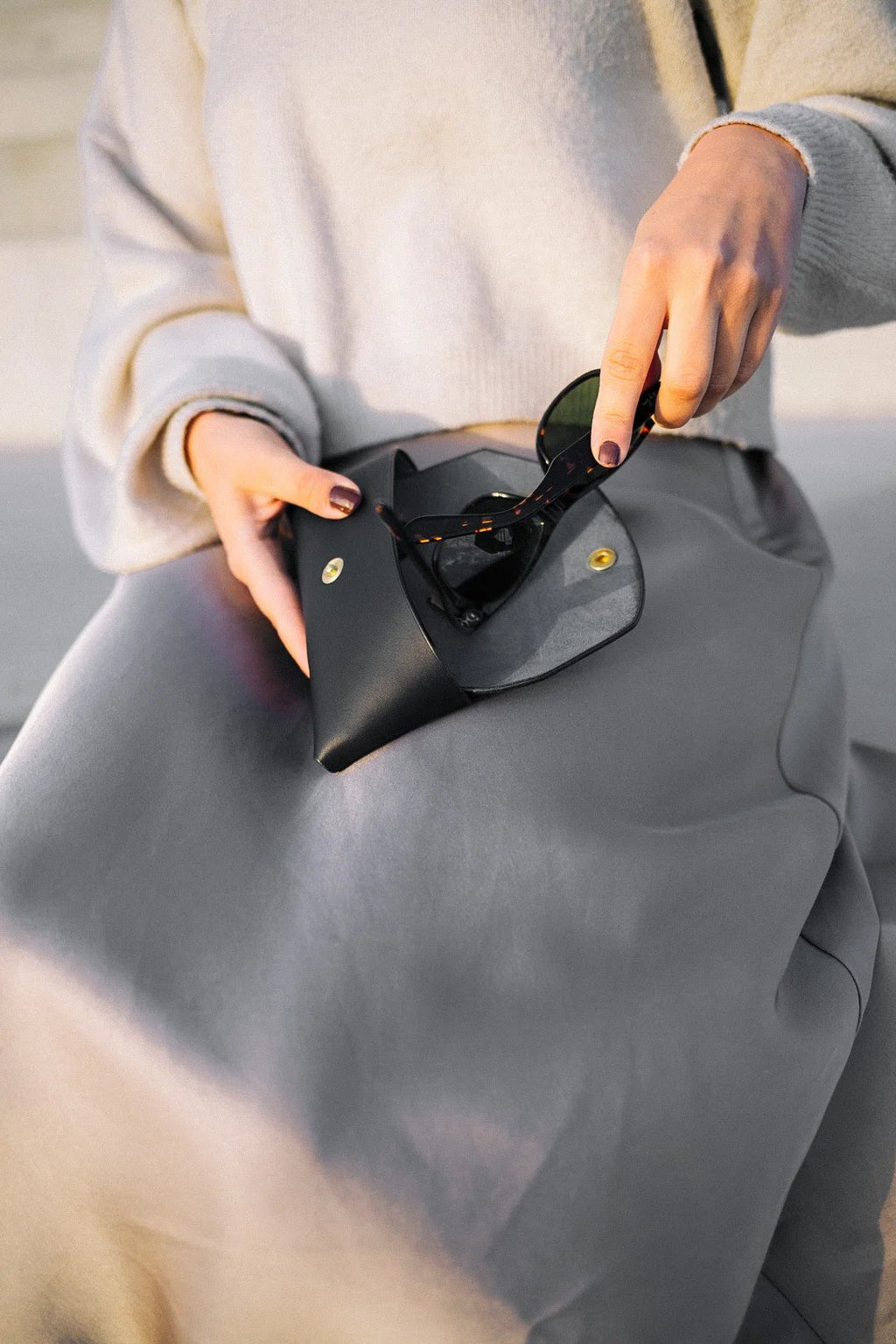 4. Woman removing sunglasses from Mirgoods black leather case, emphasizing durable construction, lifestyle setting
