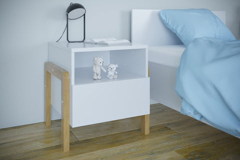 1. Kocot Kids Victor bedside table in bedroom with blue bedding, featuring white finish and oak legs, styled with lamp and toys