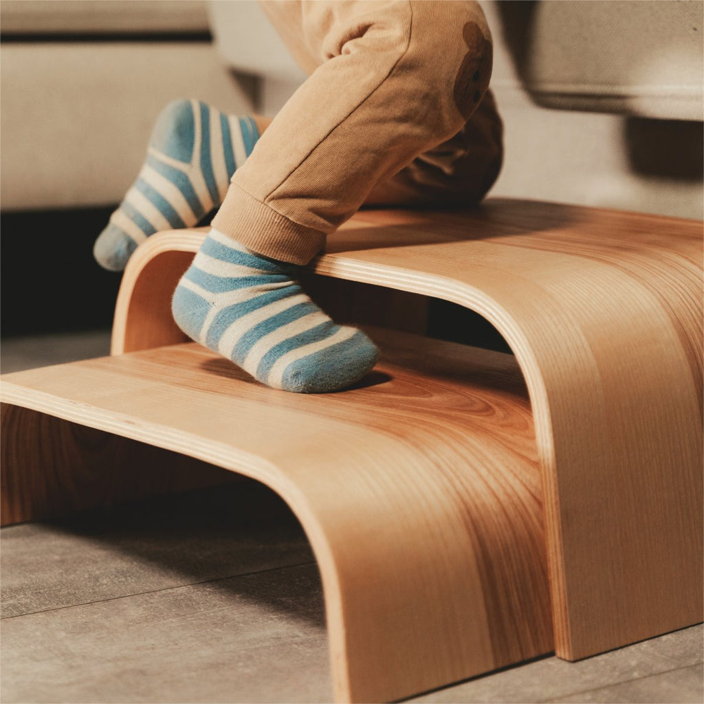 3. Close-up of child's feet on wooden step stool with striped socks indoors