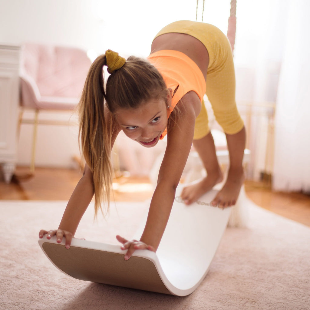 1. Girl balancing on white board in living room, wearing yellow outfit, showcasing playfulness