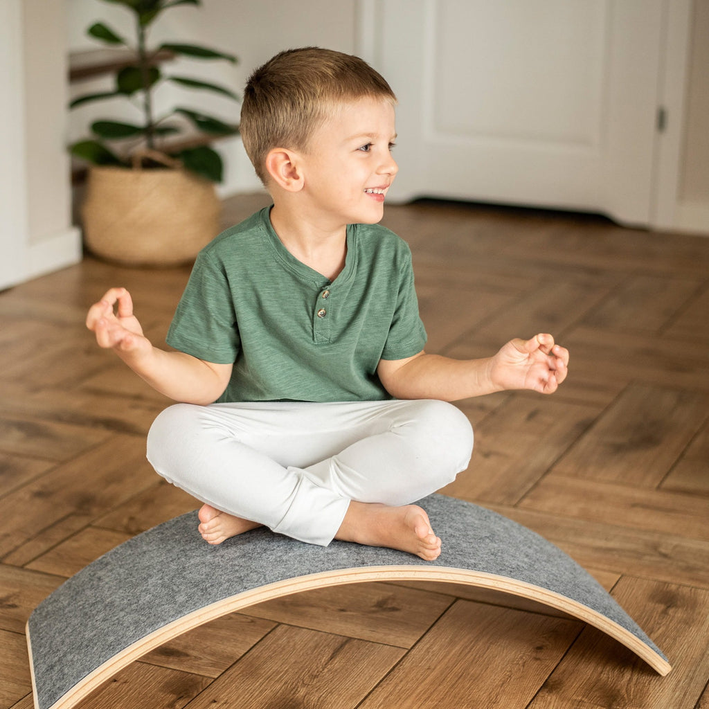 1. Boy sitting cross-legged on grey balance board in living room, practicing balance and focus