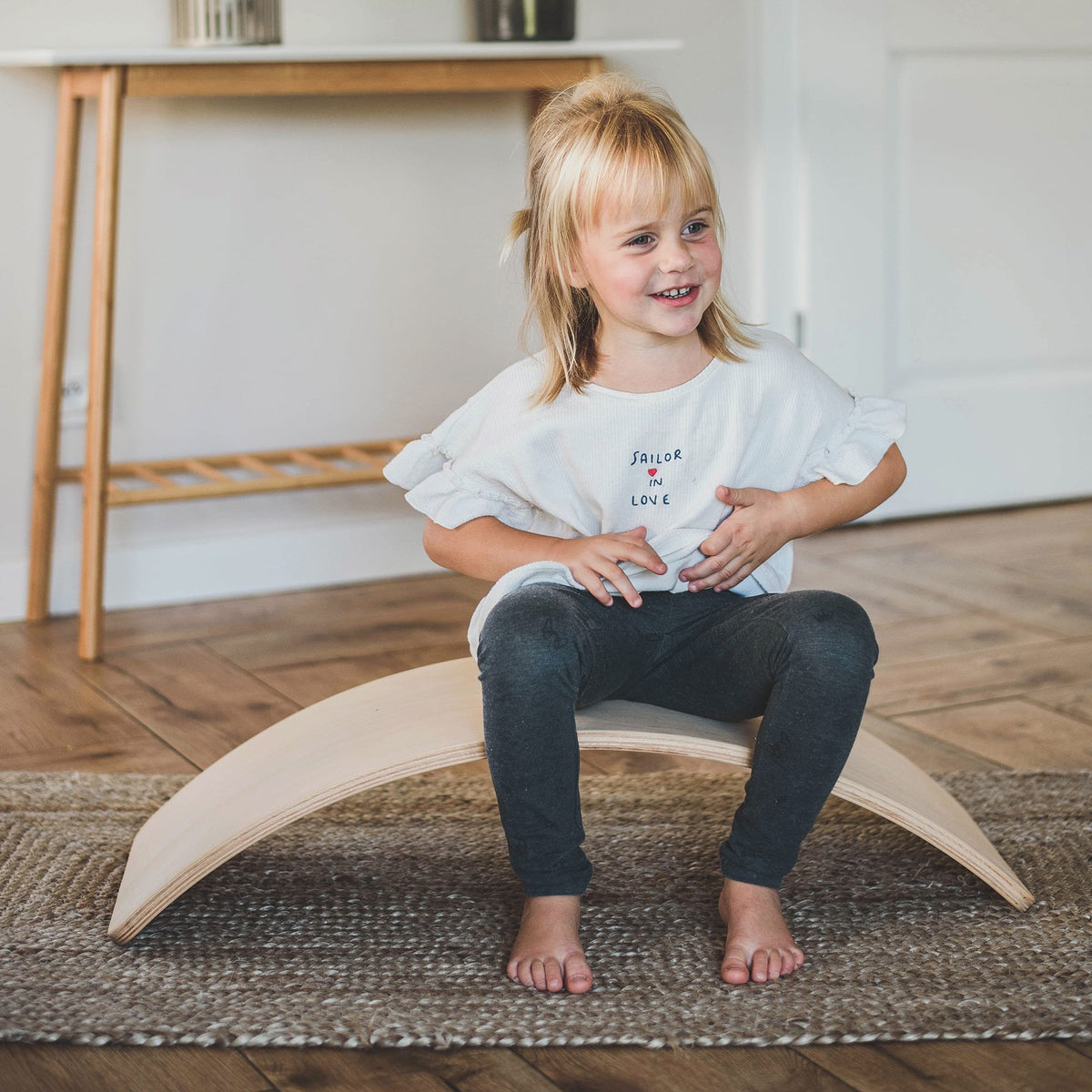 1. Child sitting on beige balance board in living room, smiling and playing, showcasing versatility