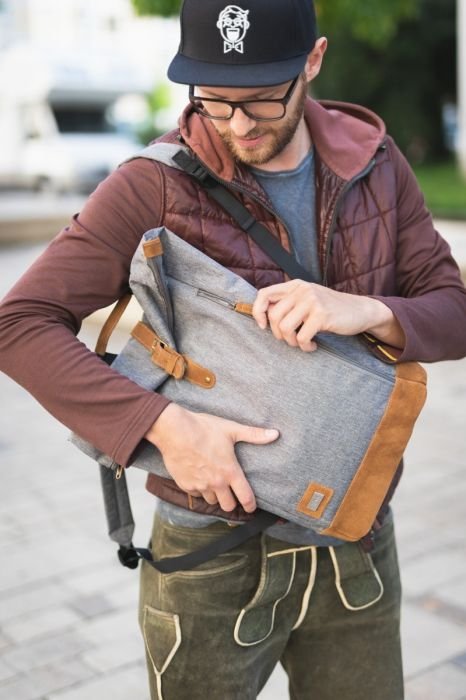 1. Man wearing a cap and brown jacket adjusting grey Fillikid diaper backpack with brown accents on urban street