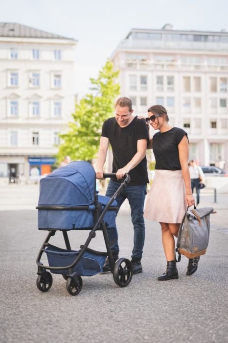 1. Couple with stroller, woman holding grey Fillikid diaper backpack, walking in city setting