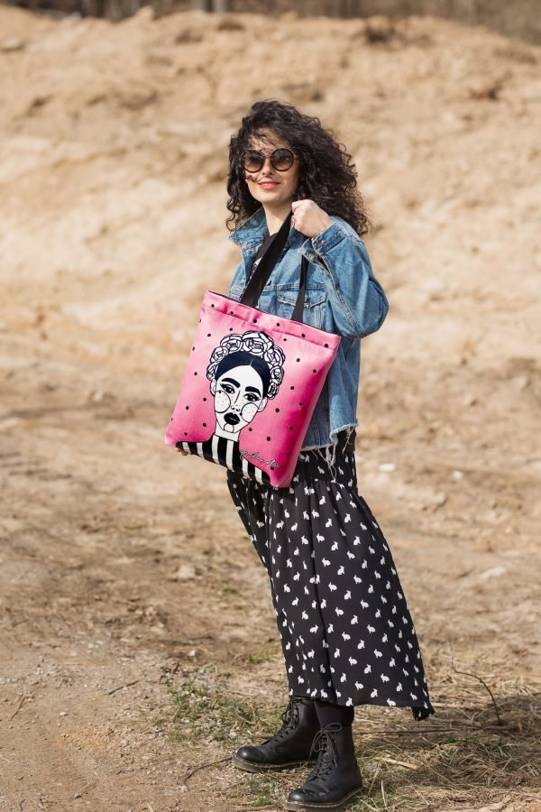 2. Woman wearing denim jacket carrying Garbanota HANDBAG MARGO in pink with graphic art outdoors