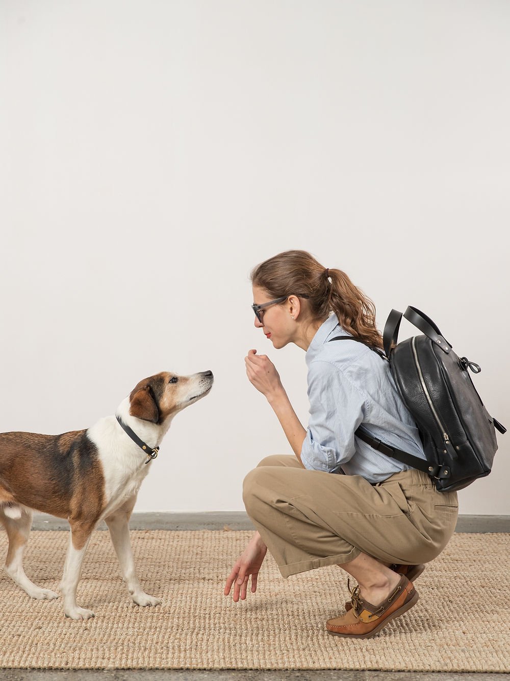 4. Woman crouching with TOKS VISOKS GORDON Backpack in dark denim, interacting with dog, showcasing lifestyle use